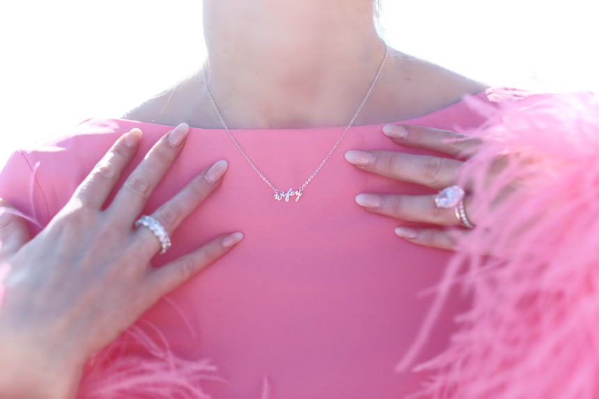 Close-up of Charlotte’s wifey necklace, rings, and pink feather-trimmed sleeves