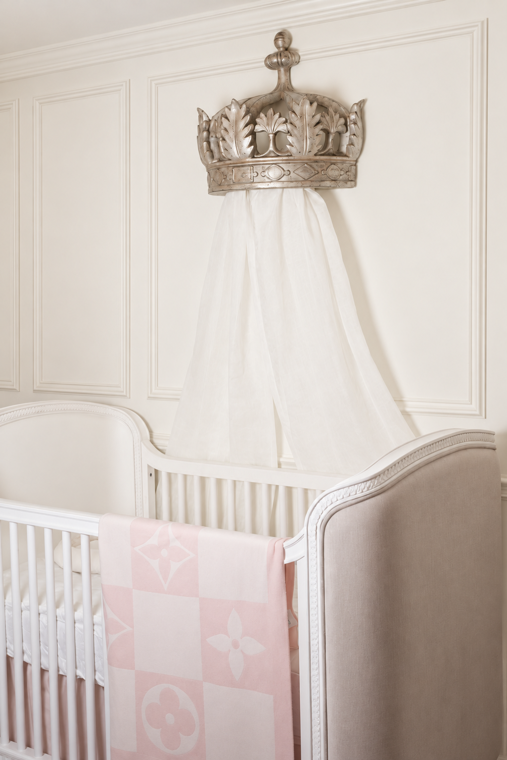A closer view of the ornate crown and white canopy above Madison’s ivory Belle crib and pale pink blanket.