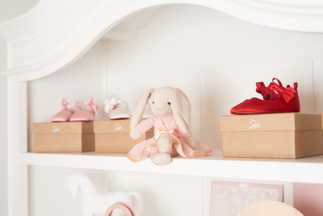 Tiny pink, ivory, and red bow shoes on keepsake boxes beside a soft blush bunny on Madison’s white bookcase.