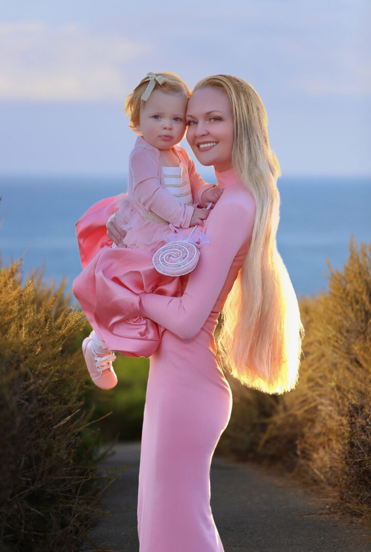 Charlotte holding Mini beside the ocean in Newport Coast, both dressed in pink