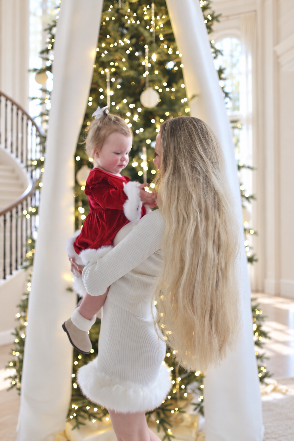 Charlotte and her daughter looking toward each other beside the Christmas tree.