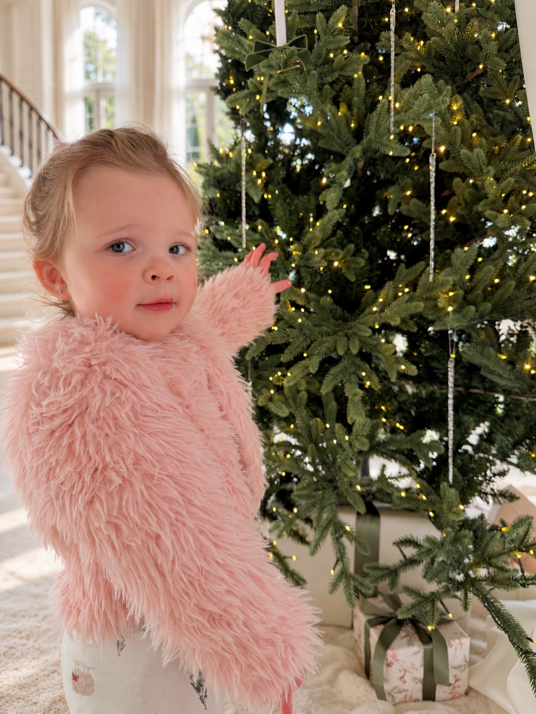 Charlotte’s daughter in a fluffy pink jacket beside the Christmas tree and ribbon-wrapped presents.