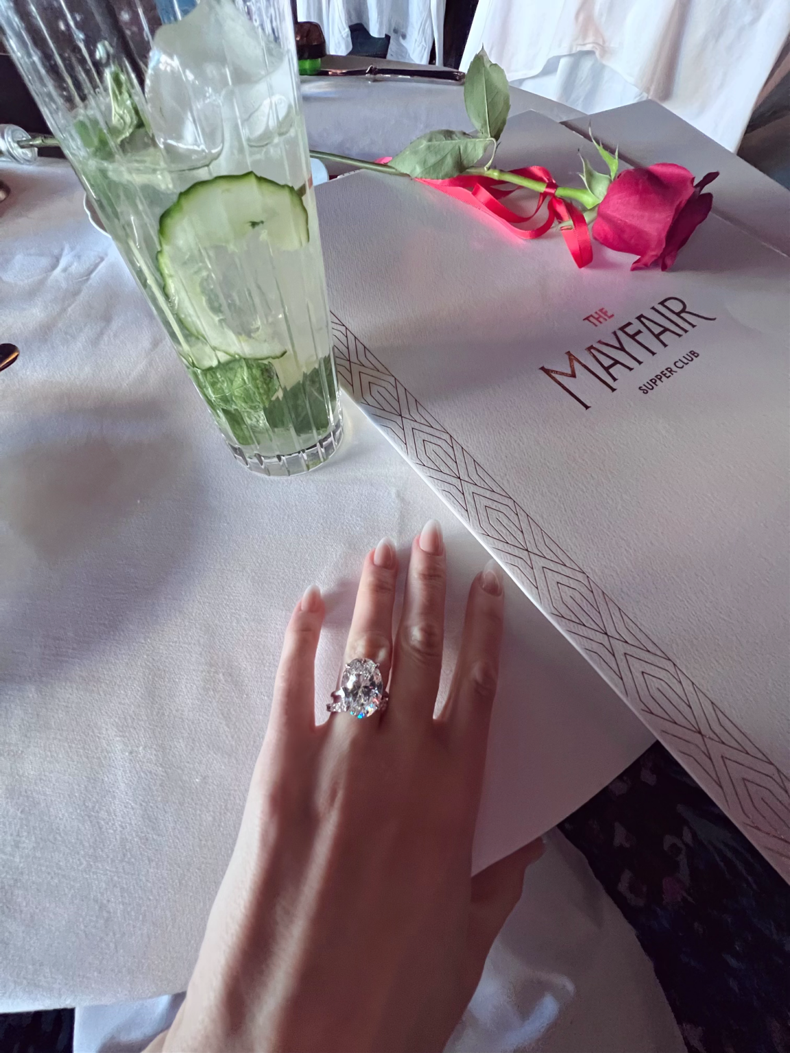 The Mayfair Supper Club menu, a red rose, and a drink on a white tablecloth